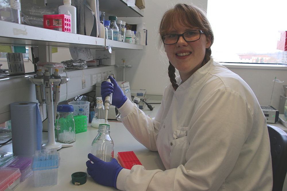 Abi Hay in the lab wearing a lab coat pipetting from a bottle