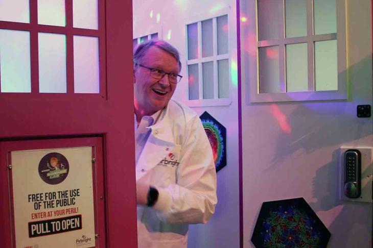 A smiling scientist in a white lab coat steps out of the door of the Dr Zoo&#039;s Viral Survival pink TARDIS