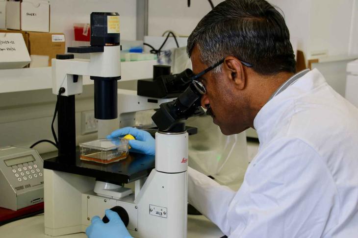 Professor Venu Nair looking down a microscope