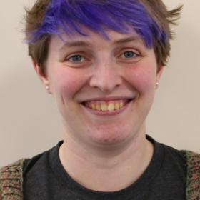 Lizzie Billington smiling broadly, she has short cropped hair with a bright purple fringe