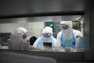 Three scientists wearing full personal protective equipment in laboratory environment.